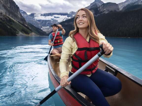 Mountaineer Lodge Lake Louise summer getaway—couple canoeing on turquoise lake with glacier views, showcasing hotel deal with free breakfast.