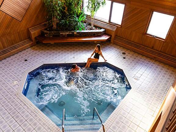 Bird's Eye View of male guest sitting in the hot tub at Mountaineer Lodge, warming up while female guest relaxes on the edge.