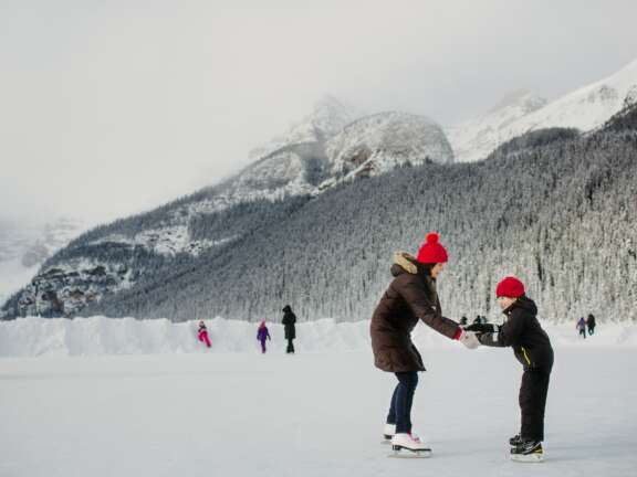 Mother helps child learn how to skate on Lake Louise, Alberta near the Mountaineer Lodge