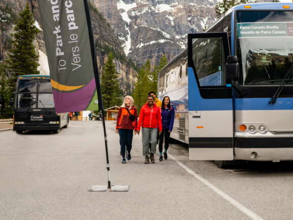 Travelers walking up to a shuttle bus with an open door with a mountain behind them.