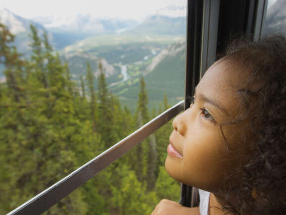 Child looking out through the window of an enclosed cabin aboard the Lake Louise Sightseeing Gondola