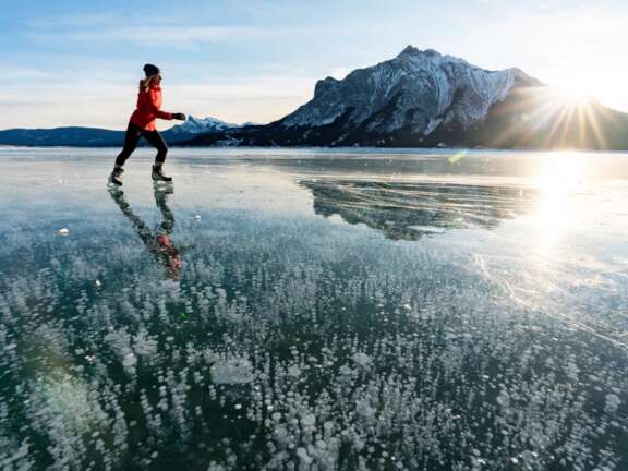 Skater skating on smooth Vermilion Lakes with sunshine and bubbles under the ice