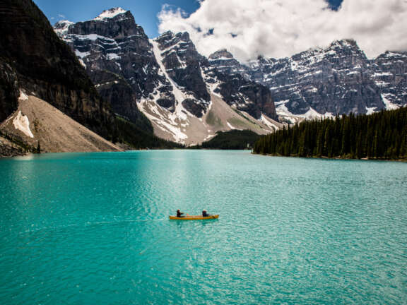2 canoers paddling in a canoe on blue water on Moraine Lake in Banff National Park in the Rocky Mountains in Canada